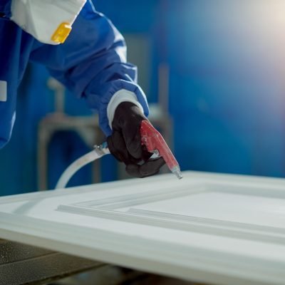 Close-up of worker spraying timber with spray gun and woodworking factory.